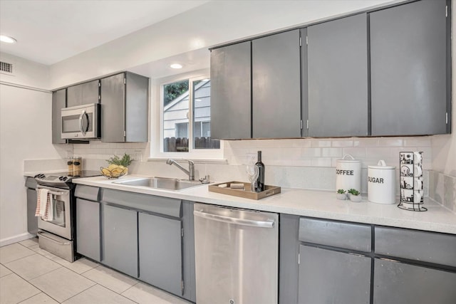 kitchen featuring light tile patterned flooring, backsplash, appliances with stainless steel finishes, gray cabinets, and sink