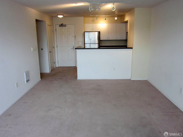 unfurnished living room featuring light carpet, visible vents, and track lighting