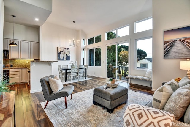 living area featuring dark wood-style floors, a notable chandelier, baseboards, and a towering ceiling