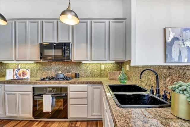 kitchen with tasteful backsplash, wood finished floors, hanging light fixtures, black appliances, and a sink