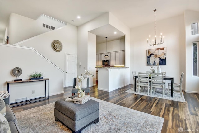 living room with dark wood-style floors, visible vents, baseboards, a high ceiling, and a notable chandelier