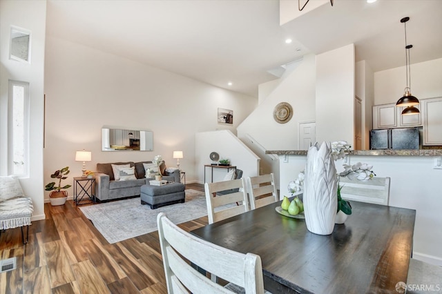 dining room featuring wood finished floors, visible vents, baseboards, stairs, and a towering ceiling