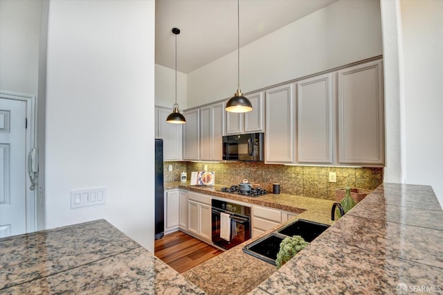 kitchen featuring tasteful backsplash, decorative light fixtures, light wood-type flooring, black appliances, and a sink