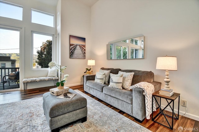 living area featuring visible vents, wood finished floors, baseboards, and a towering ceiling