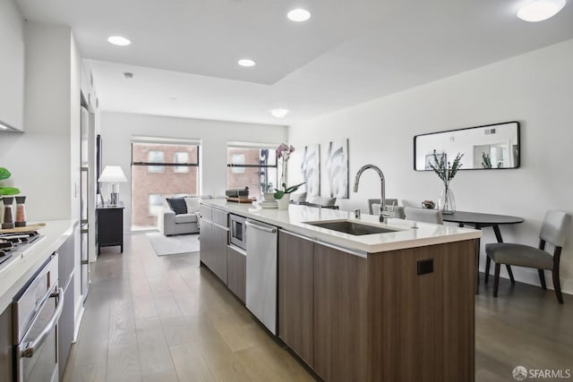 kitchen with light countertops, appliances with stainless steel finishes, a sink, an island with sink, and modern cabinets