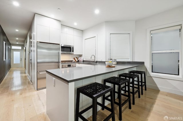 kitchen featuring light wood-type flooring, kitchen peninsula, white cabinetry, appliances with stainless steel finishes, and a kitchen breakfast bar