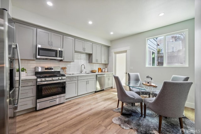 kitchen featuring appliances with stainless steel finishes, sink, light hardwood / wood-style flooring, and gray cabinetry