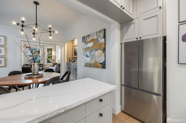 kitchen with light stone counters, freestanding refrigerator, hanging light fixtures, white cabinetry, and a notable chandelier