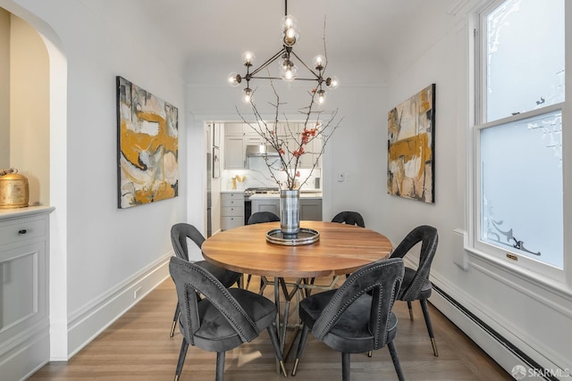 dining space featuring arched walkways, light wood finished floors, a baseboard radiator, an inviting chandelier, and baseboards