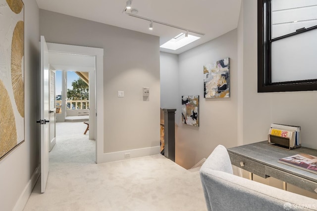 hallway with rail lighting, light colored carpet, an upstairs landing, and a skylight