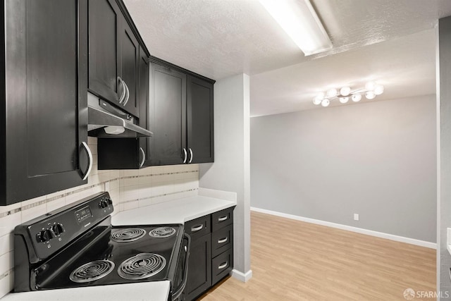 kitchen featuring light countertops, black range with electric cooktop, under cabinet range hood, and dark cabinets