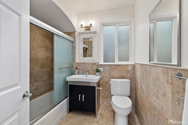 full bathroom with vanity, combined bath / shower with glass door, tile walls, and toilet