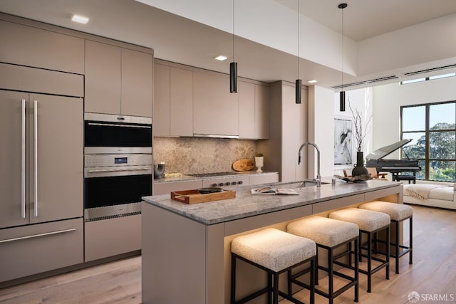 kitchen featuring stainless steel double oven, built in fridge, gray cabinetry, a sink, and light wood-type flooring