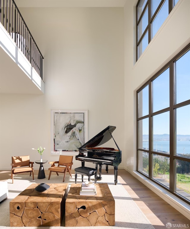 sitting room featuring baseboards, a water view, a high ceiling, and wood finished floors