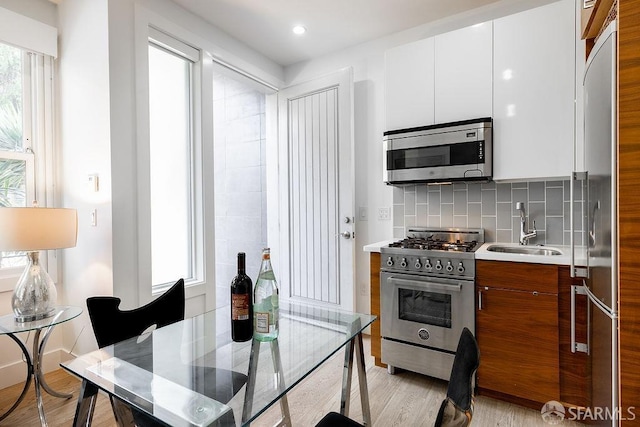 kitchen with tasteful backsplash, appliances with stainless steel finishes, light countertops, light wood-style floors, and a sink