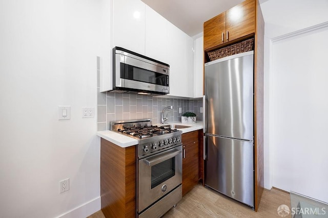 kitchen featuring tasteful backsplash, brown cabinetry, appliances with stainless steel finishes, light countertops, and a sink
