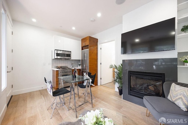 kitchen featuring stainless steel appliances, light wood-style floors, light countertops, tasteful backsplash, and a glass covered fireplace