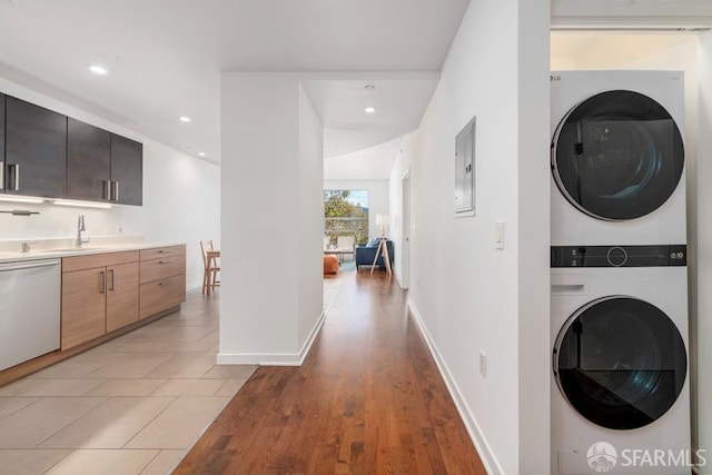 clothes washing area with light hardwood / wood-style floors, stacked washing maching and dryer, electric panel, and sink