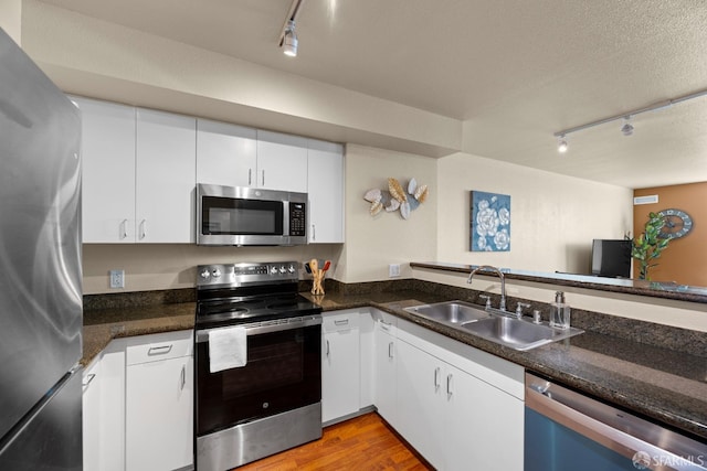 kitchen with light wood-style flooring, a sink, a textured ceiling, white cabinetry, and stainless steel appliances