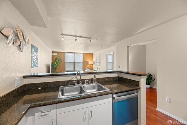 kitchen with a sink, a textured ceiling, wood finished floors, white cabinets, and dishwasher