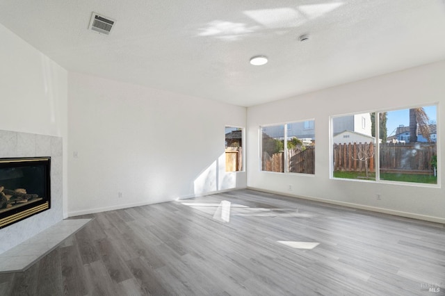 unfurnished living room featuring a healthy amount of sunlight, a tiled fireplace, wood-type flooring, and a textured ceiling