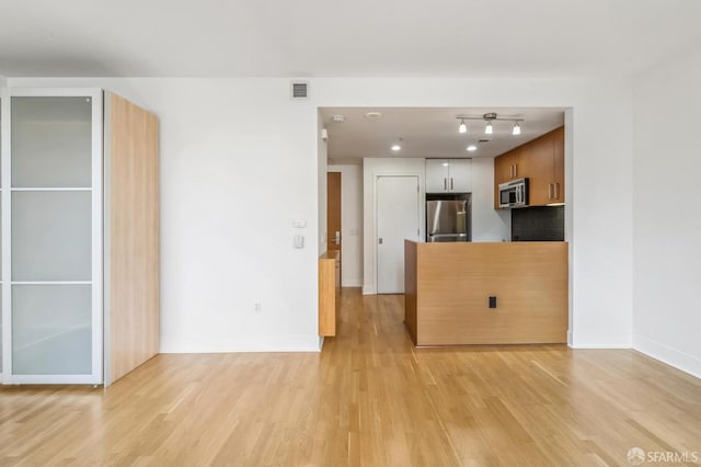 kitchen with appliances with stainless steel finishes, light wood-type flooring, and decorative backsplash