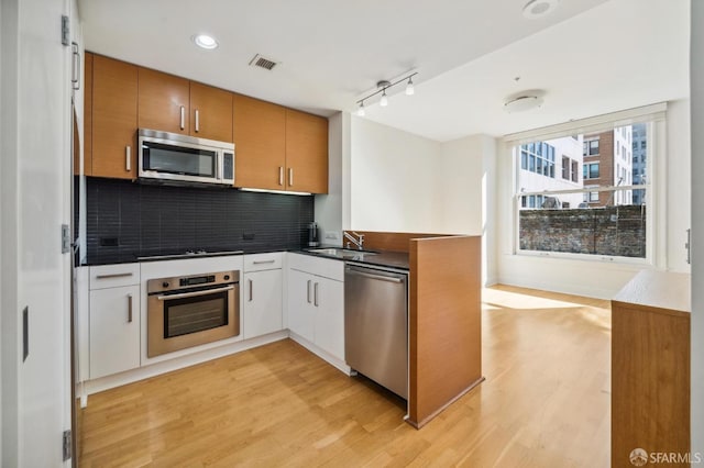 kitchen with stainless steel appliances, sink, white cabinets, light hardwood / wood-style floors, and tasteful backsplash