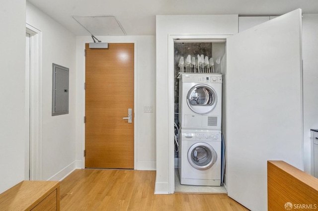 laundry room featuring electric panel, stacked washer and dryer, and light wood-type flooring