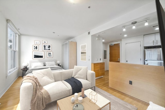 bedroom featuring stainless steel fridge, track lighting, electric panel, and light hardwood / wood-style floors