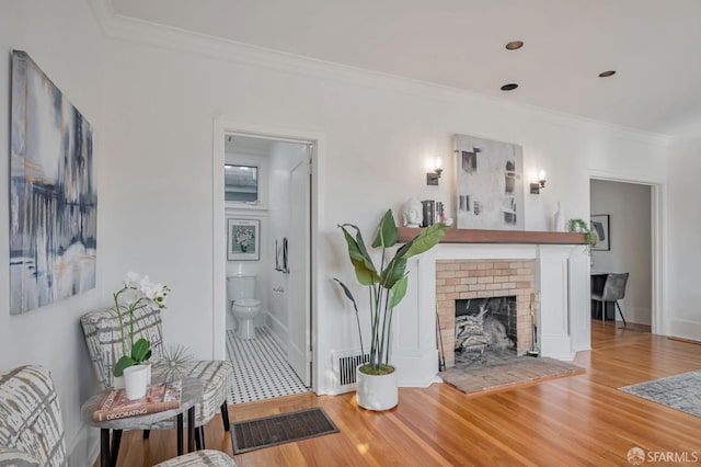 living area featuring visible vents, a brick fireplace, crown molding, and wood finished floors