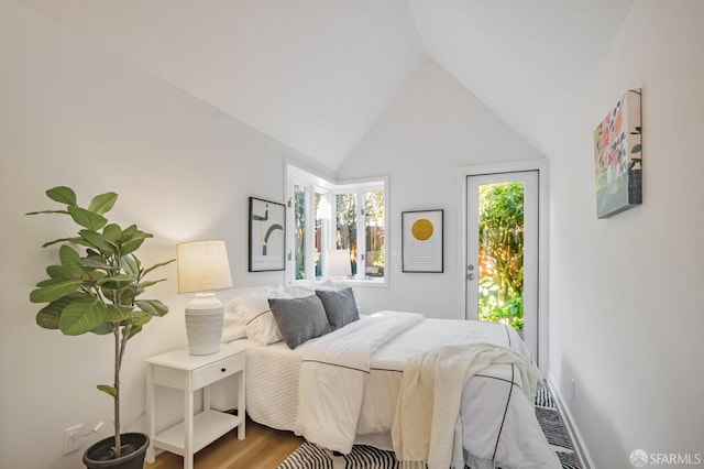 bedroom featuring access to exterior, vaulted ceiling, and wood finished floors