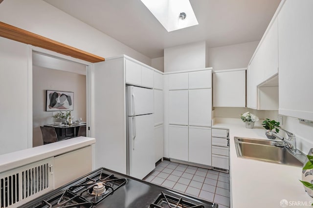 kitchen featuring white cabinetry, a skylight, freestanding refrigerator, and a sink