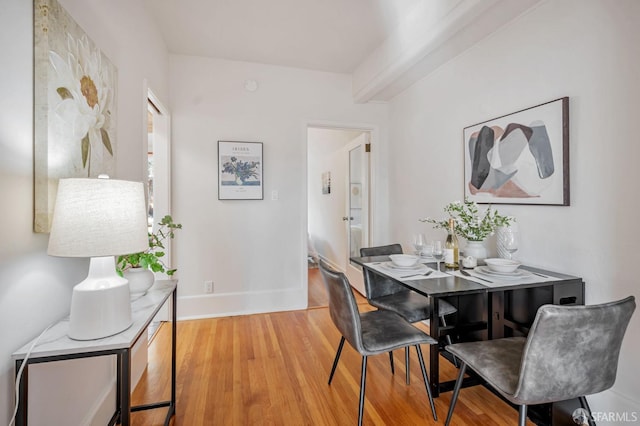 dining area with beam ceiling, baseboards, and light wood finished floors