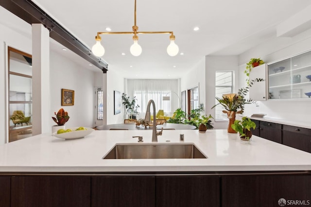 kitchen featuring decorative light fixtures, dark brown cabinets, a center island with sink, and sink