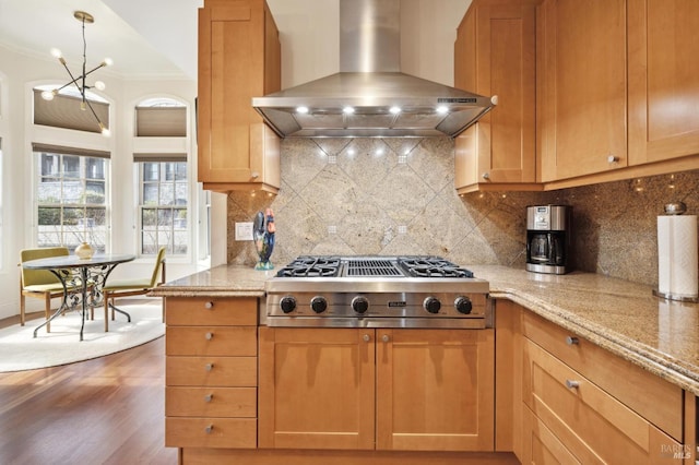 kitchen with stainless steel gas stovetop, light stone counters, wall chimney range hood, and tasteful backsplash