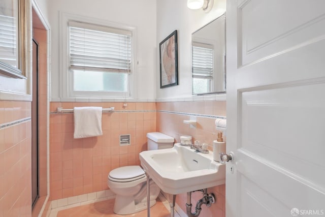 bathroom with sink, a shower with shower door, toilet, tile patterned floors, and tile walls