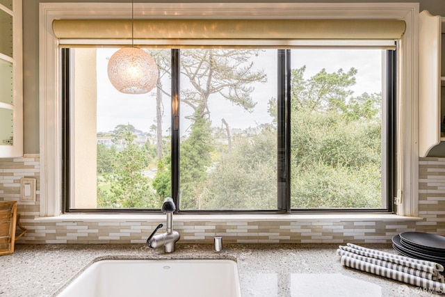 room details featuring backsplash, light stone countertops, and pendant lighting