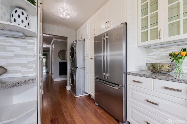 kitchen with stacked washer and clothes dryer, white cabinetry, dark hardwood / wood-style flooring, stainless steel refrigerator, and decorative backsplash