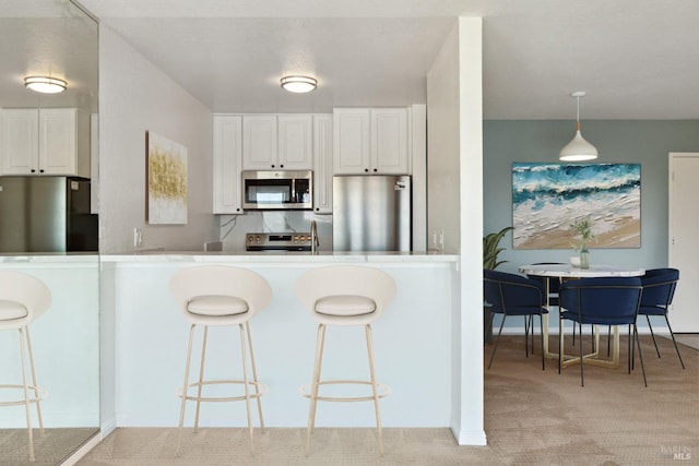 kitchen with appliances with stainless steel finishes, white cabinetry, decorative light fixtures, and a kitchen breakfast bar