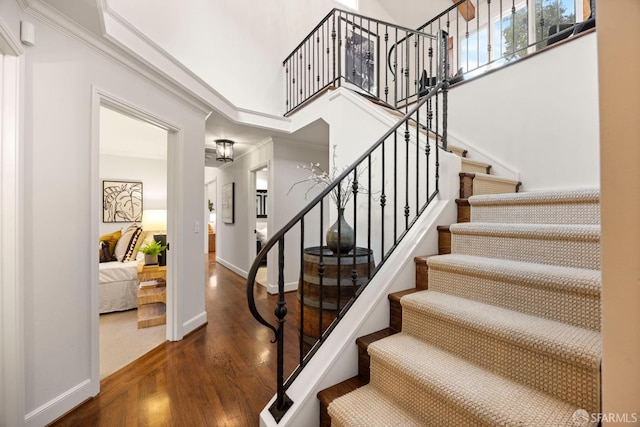 staircase featuring ornamental molding, wood finished floors, a towering ceiling, and baseboards