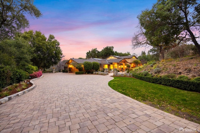 view of front of home with decorative driveway and a yard