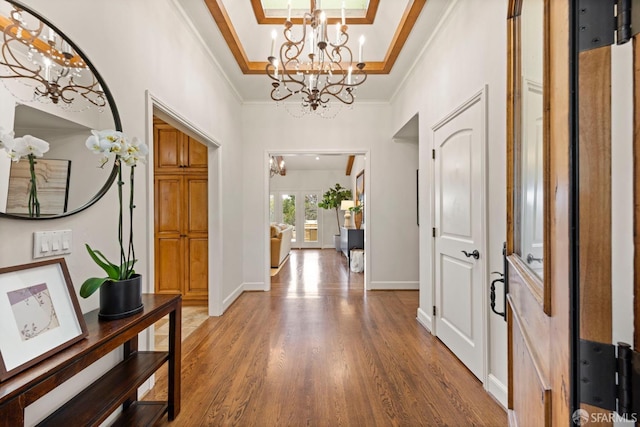 entryway featuring baseboards, a raised ceiling, ornamental molding, wood finished floors, and a notable chandelier