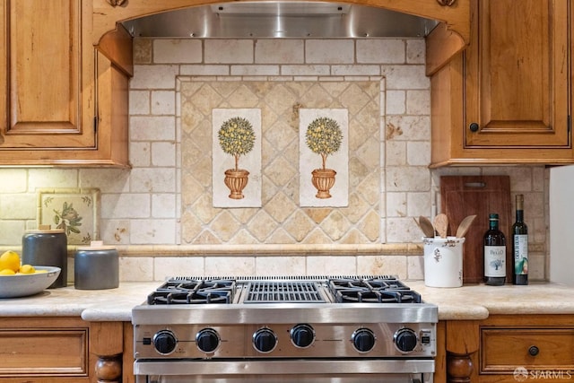 kitchen with under cabinet range hood, stove, brown cabinets, and backsplash