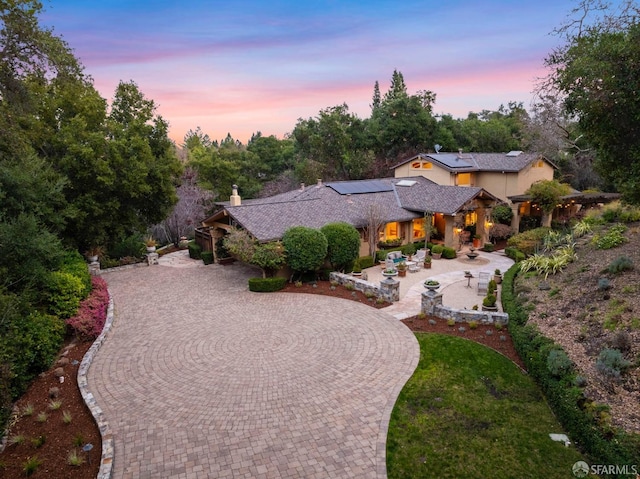 view of front facade featuring a chimney, curved driveway, a patio area, roof mounted solar panels, and stucco siding