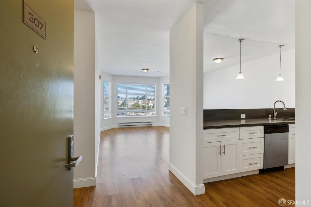 interior space with pendant lighting, white cabinets, dishwasher, a baseboard radiator, and hardwood / wood-style floors