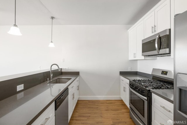 kitchen with hanging light fixtures, white cabinetry, stainless steel appliances, hardwood / wood-style floors, and sink