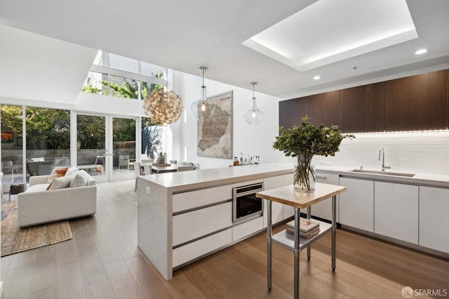 kitchen with pendant lighting, white cabinetry, sink, stainless steel oven, and light hardwood / wood-style flooring