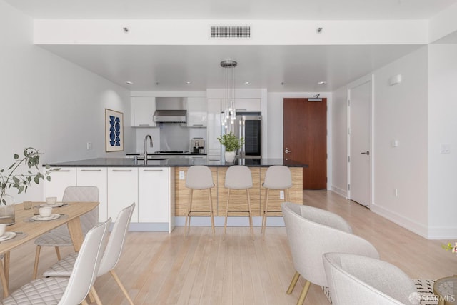 kitchen with hanging light fixtures, sink, white cabinetry, ventilation hood, and light wood-type flooring