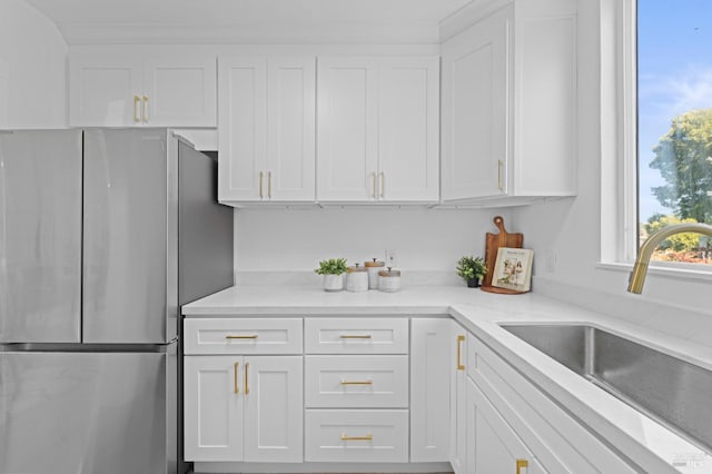 kitchen featuring light stone counters, freestanding refrigerator, white cabinetry, and a sink