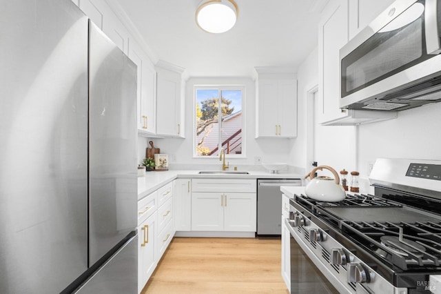 kitchen with white cabinetry, stainless steel appliances, a sink, and light countertops